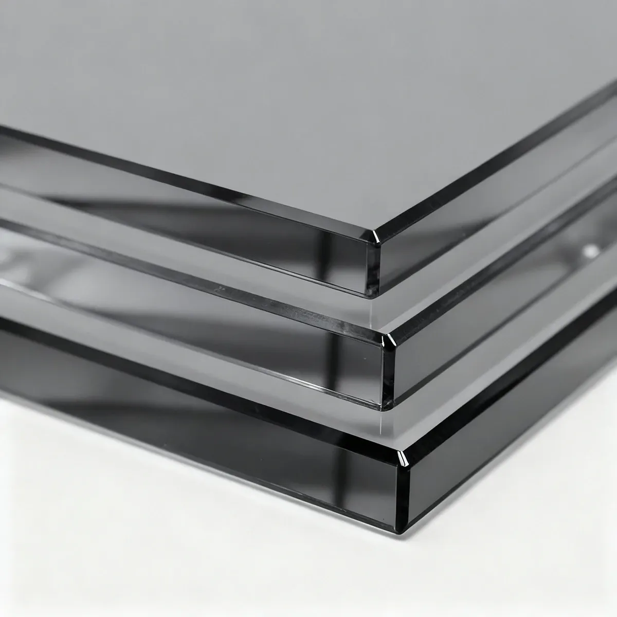 A close-up shot of three stacked panels of thick, grey-tinted glass, highlighting their polished and beveled edges.