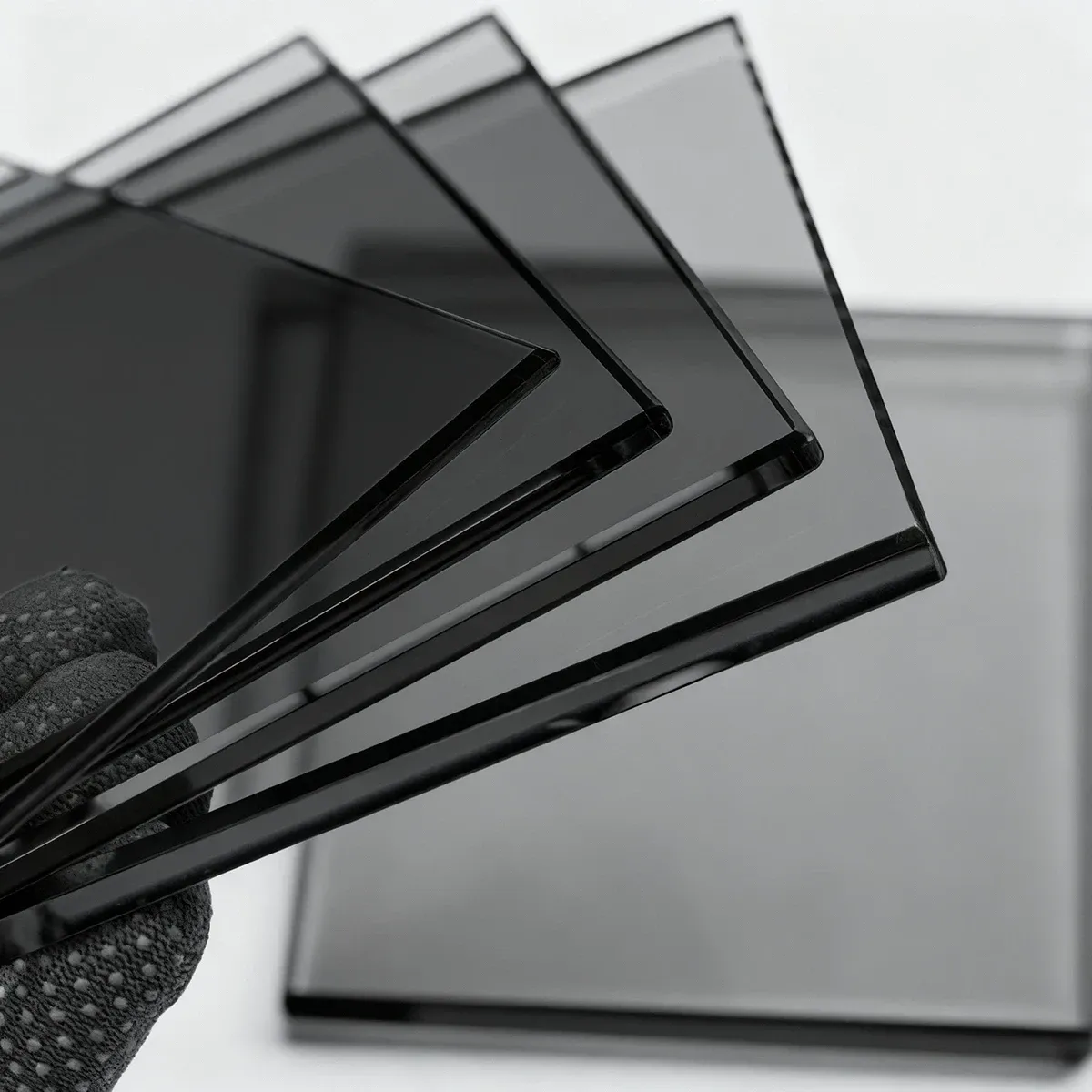 gloved hand holds a fan of several small, rectangular samples of grey-tinted glass, showing the consistent color and transparency.