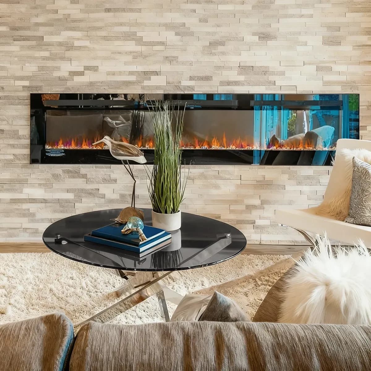 A modern living room featuring a round, dark grey-tinted glass coffee table in front of a long, wall-mounted fireplace on a stacked stone wall.