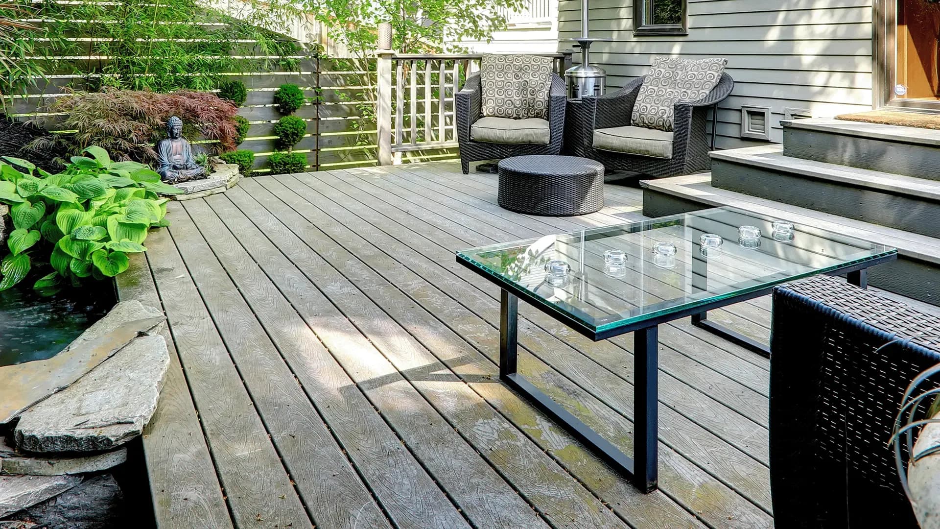 Wood deck patio with modern wicker chairs, a glass table, and a small landscaped pond.