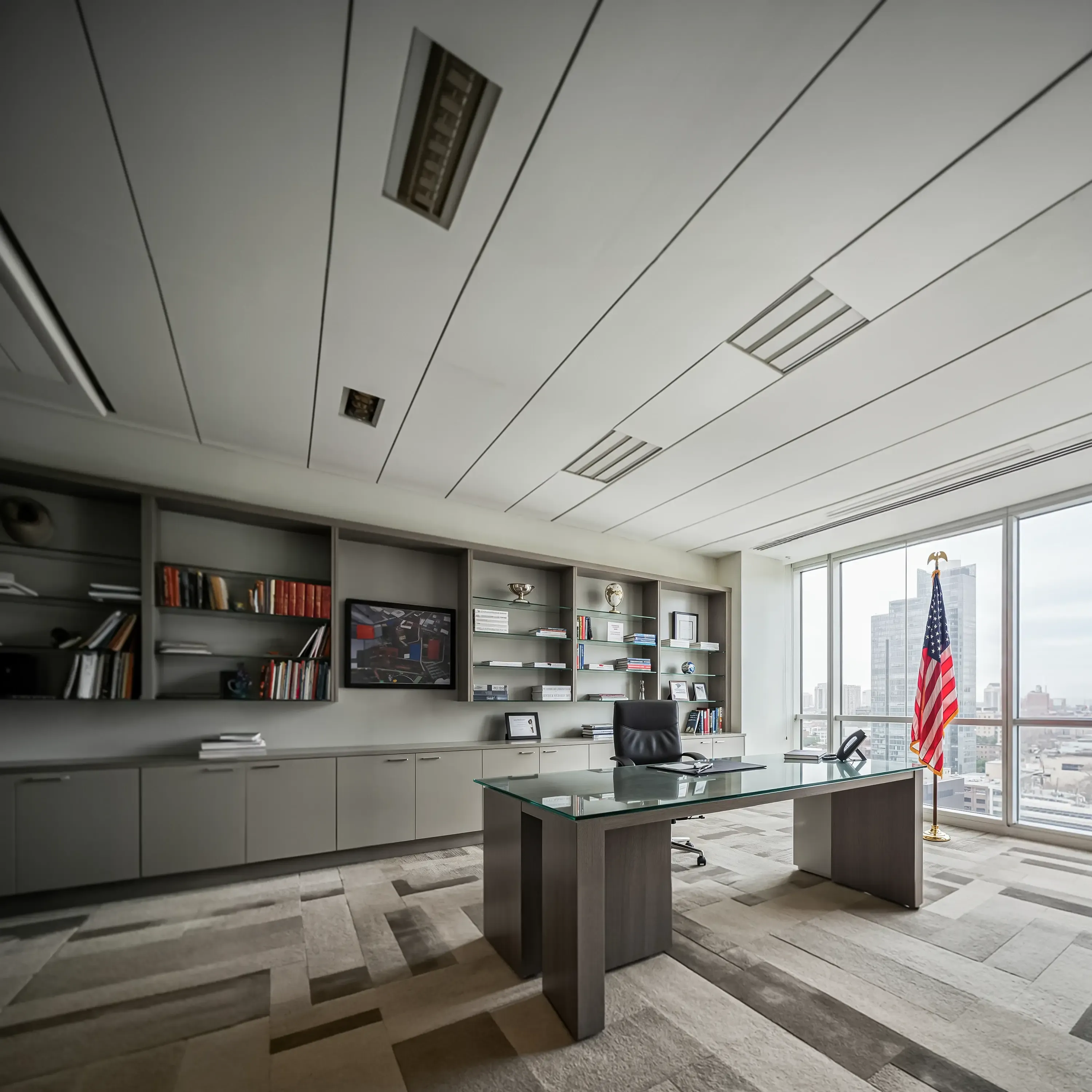 Modern executive office featuring a glass-top desk, custom built-in cabinetry, and a large window with a city view and an American flag.