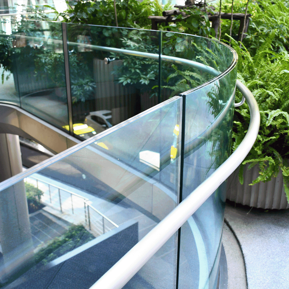 Custom glass railing with tempered glass panels and sleek curve, surrounded by greenery, showcasing modern design elements suitable for shower doors, table tops, and mirrors.