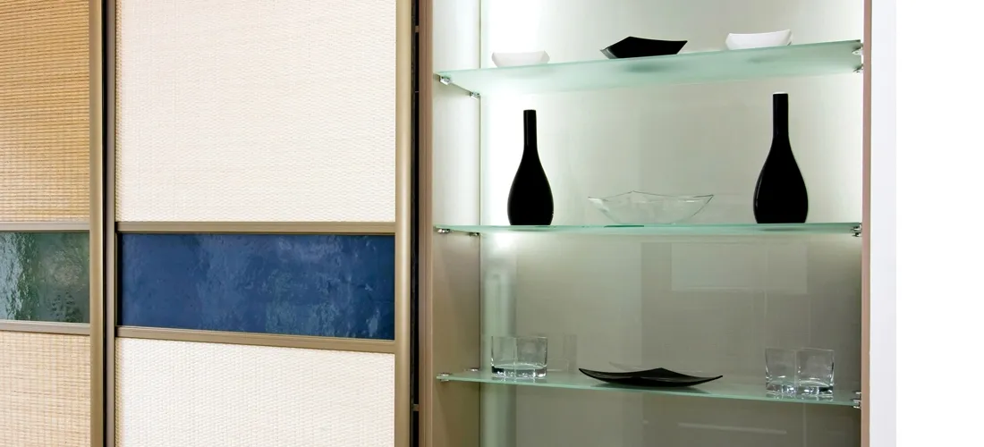 A modern display cabinet with three illuminated glass shelves holding minimalist black and clear decorative vases and bowls.