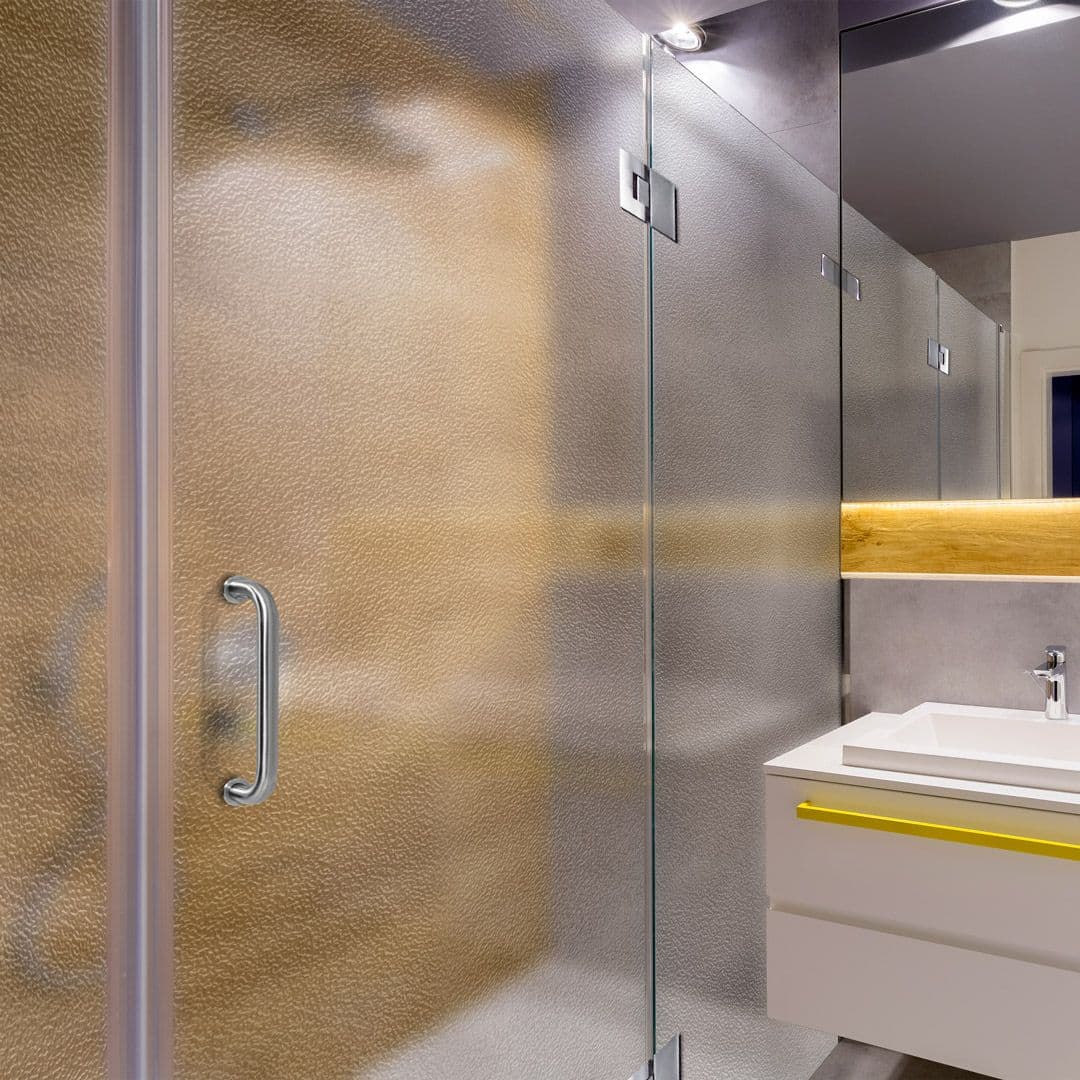 Custom glass shower doors with tempered and textured glass in a modern bathroom setting, featuring sleek design and beveled glass edge.