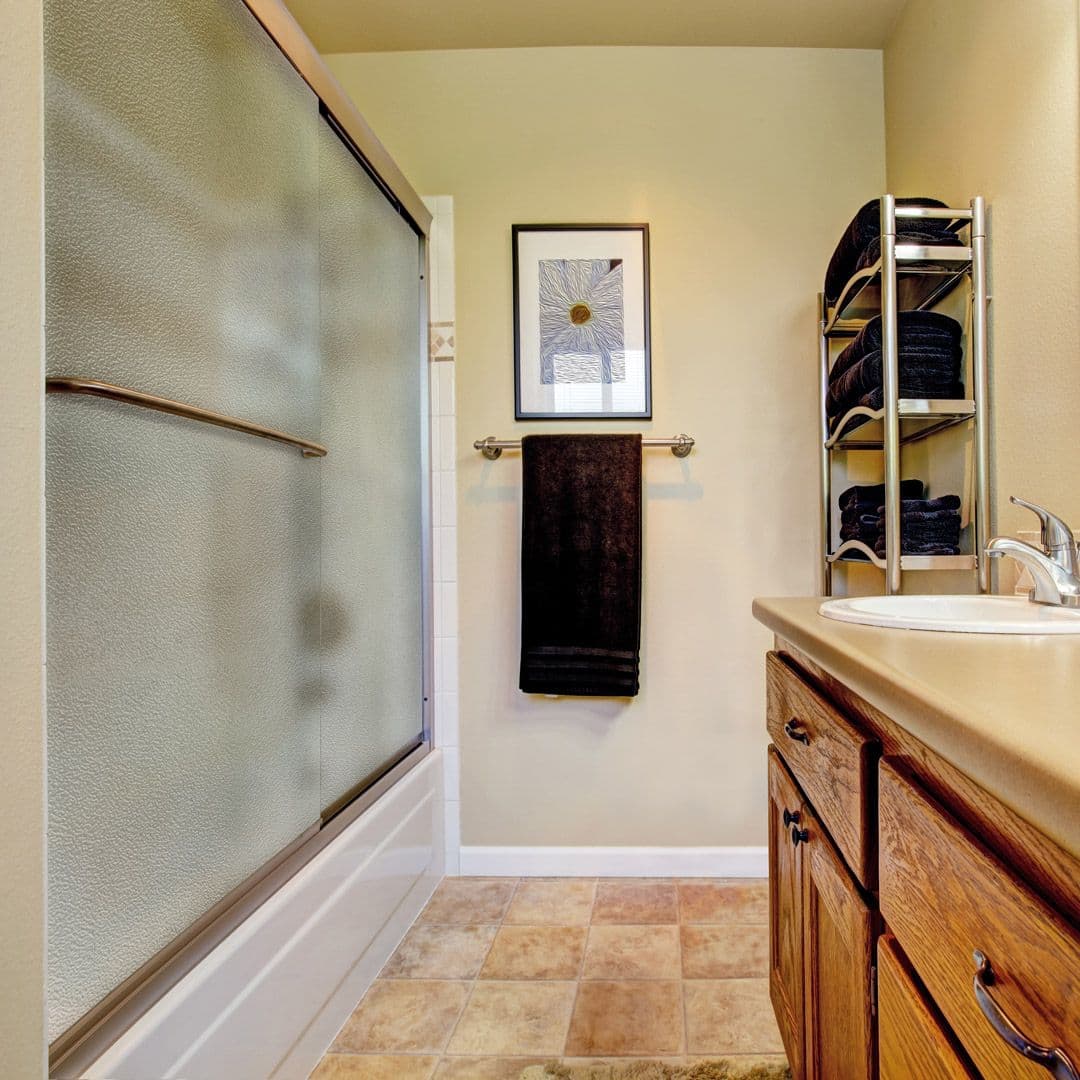 Modern bathroom featuring frosted shower doors, custom cabinetry, and organized towels, highlighting quality custom glass solutions including tempered glass for doors and mirrors.