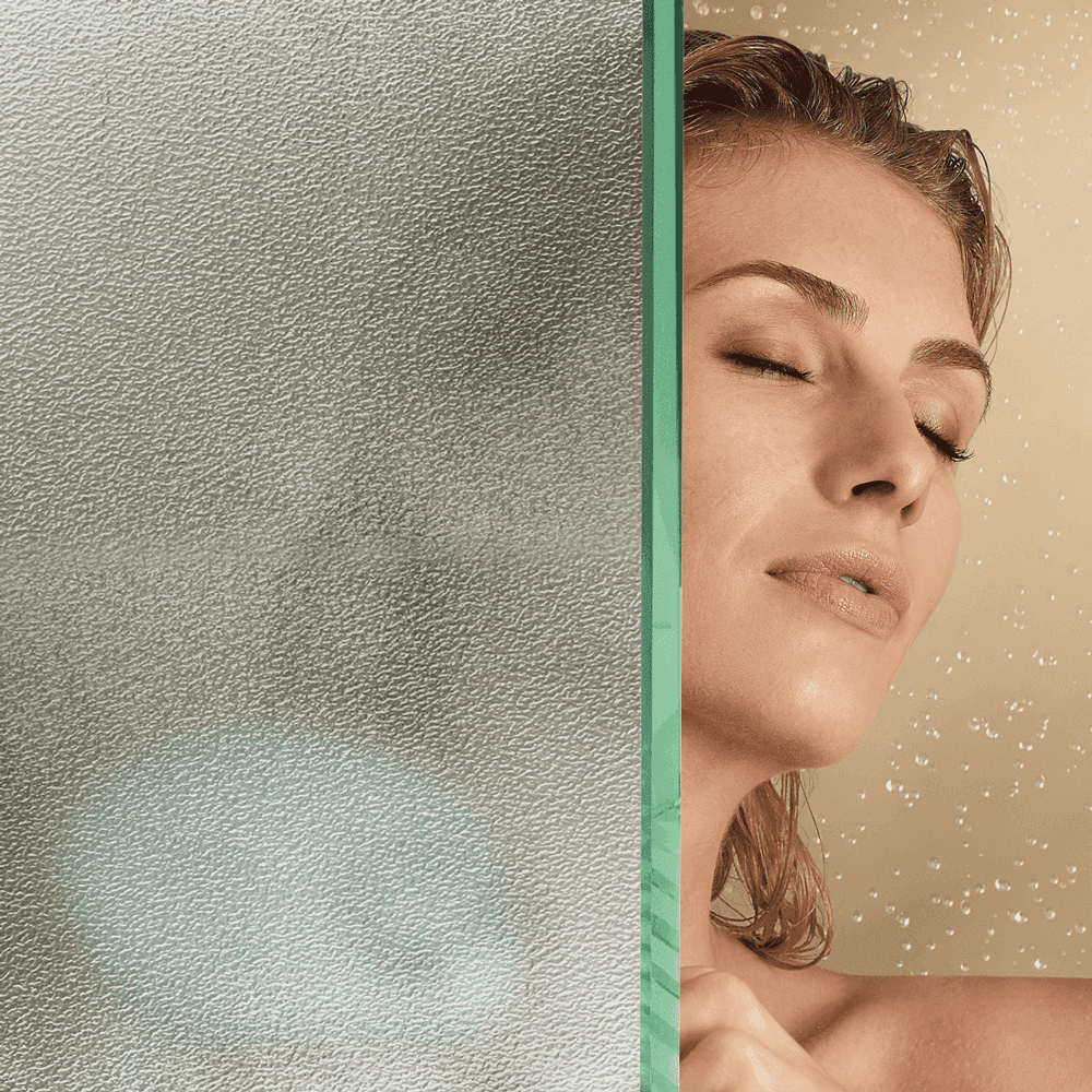 A woman enjoying a shower behind a textured custom glass shower door, highlighting its modern design and functionality, ideal for showcasing tempered and beveled glass edges.