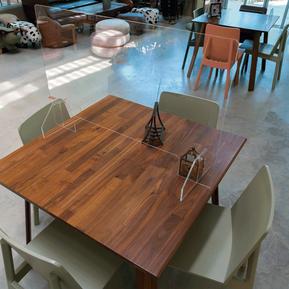 Transparent acrylic barrier on a wooden table in a restaurant setting, highlighting custom glass solutions for safety, ideal for shower doors, table tops, and mirrors.