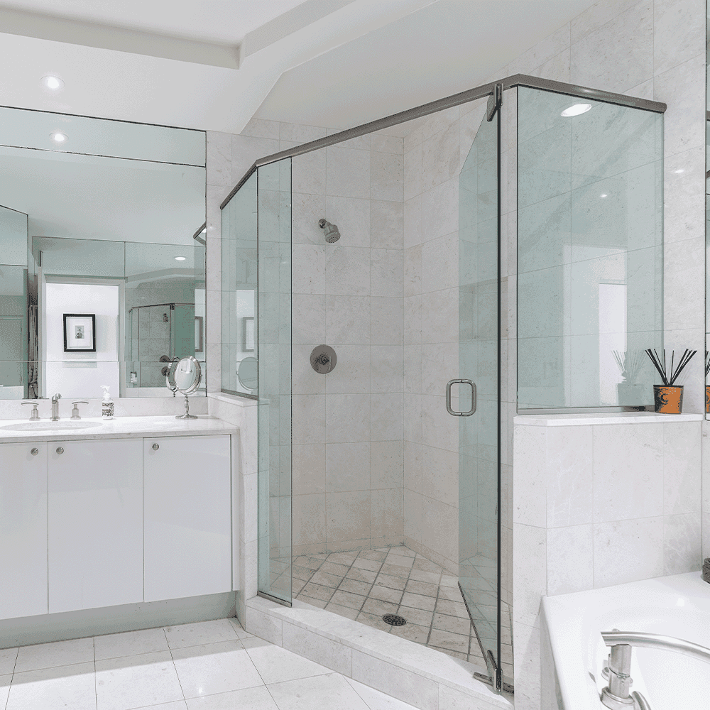 Shower doors with custom glass installation in a modern bathroom featuring beveled glass edges, mirrors, and a sleek white vanity.