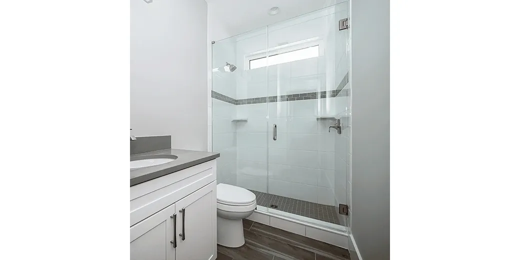 Frameless shower doors in a modern bathroom featuring custom glass design, complemented by sleek white cabinetry and a gray countertop.