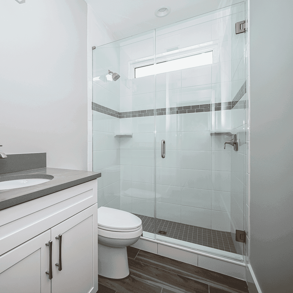 Frameless shower doors in a modern bathroom featuring custom glass design, complemented by sleek white cabinetry and a gray countertop.