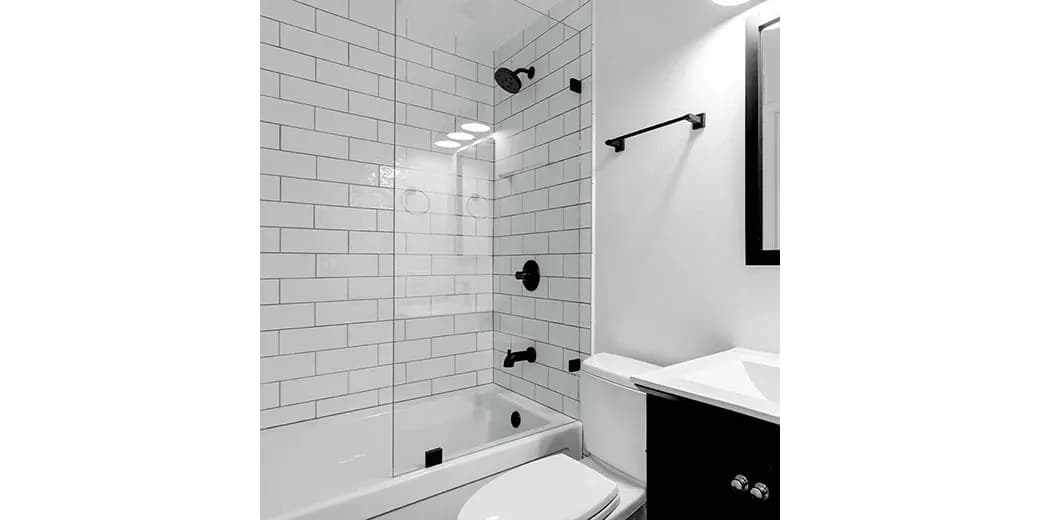 Custom glass shower doors feature a sleek design in a modern bathroom with white subway tile walls and black fixtures, showcasing tempered glass for durability and style.