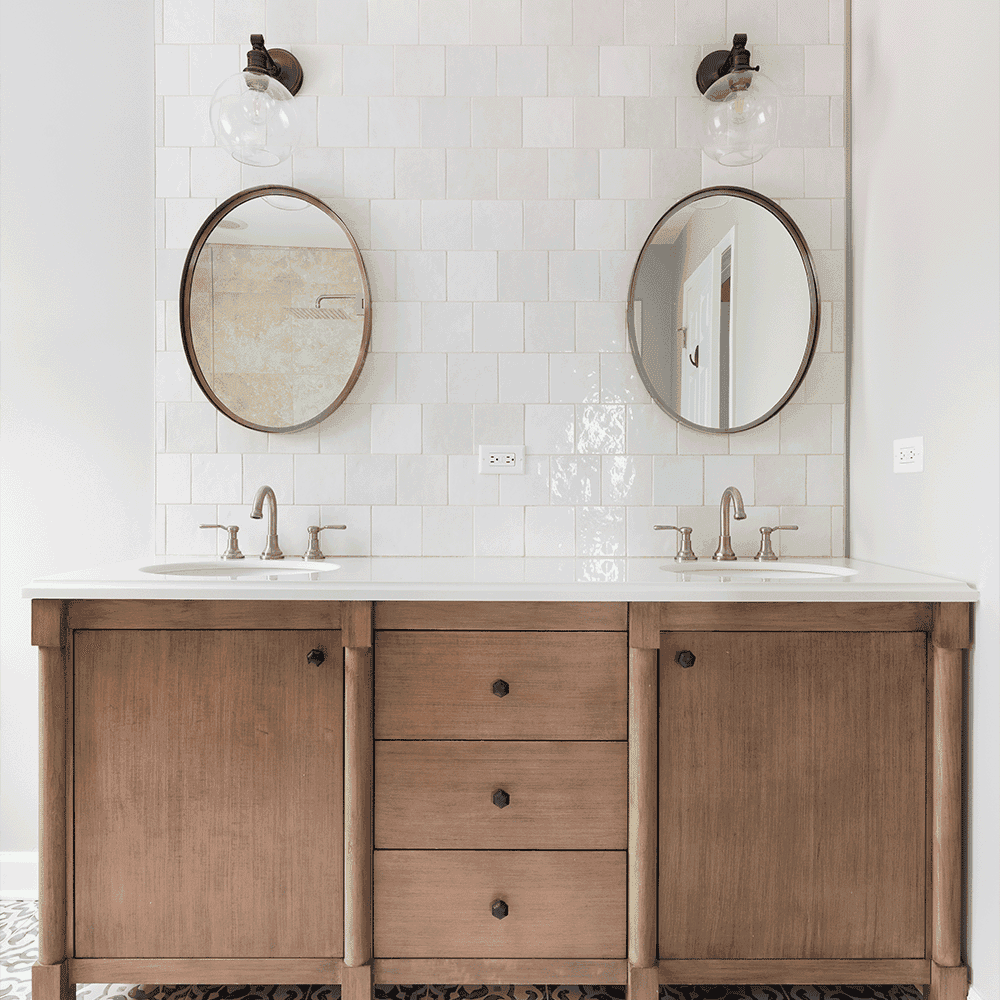 Modern bathroom featuring twin round mirrors above a custom wood vanity with a white countertop