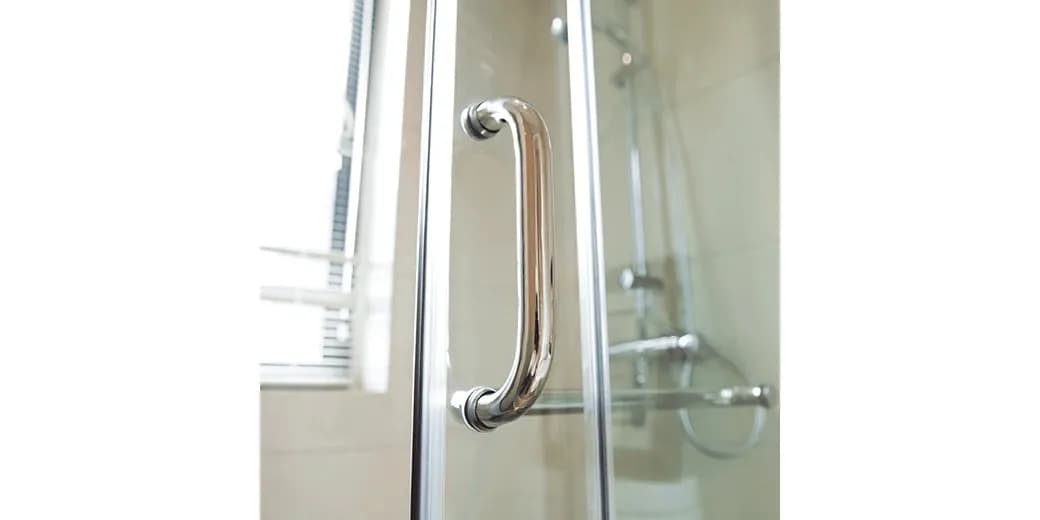 Close-up of a sleek chrome handle on a custom glass shower door, showcasing high-quality tempered glass and modern design elements.