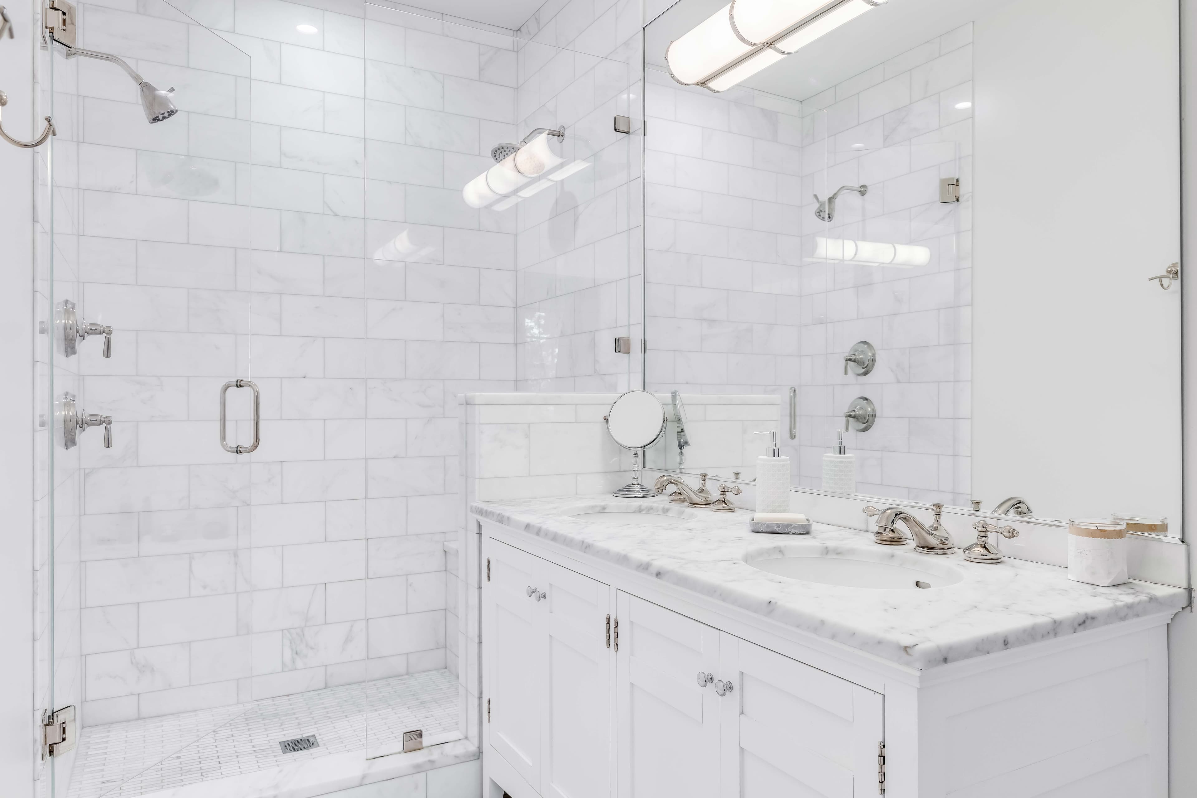 Luxury bathroom featuring custom glass shower doors, marble countertop, and mirrors, enhanced with tempered glass accents and sleek design elements.