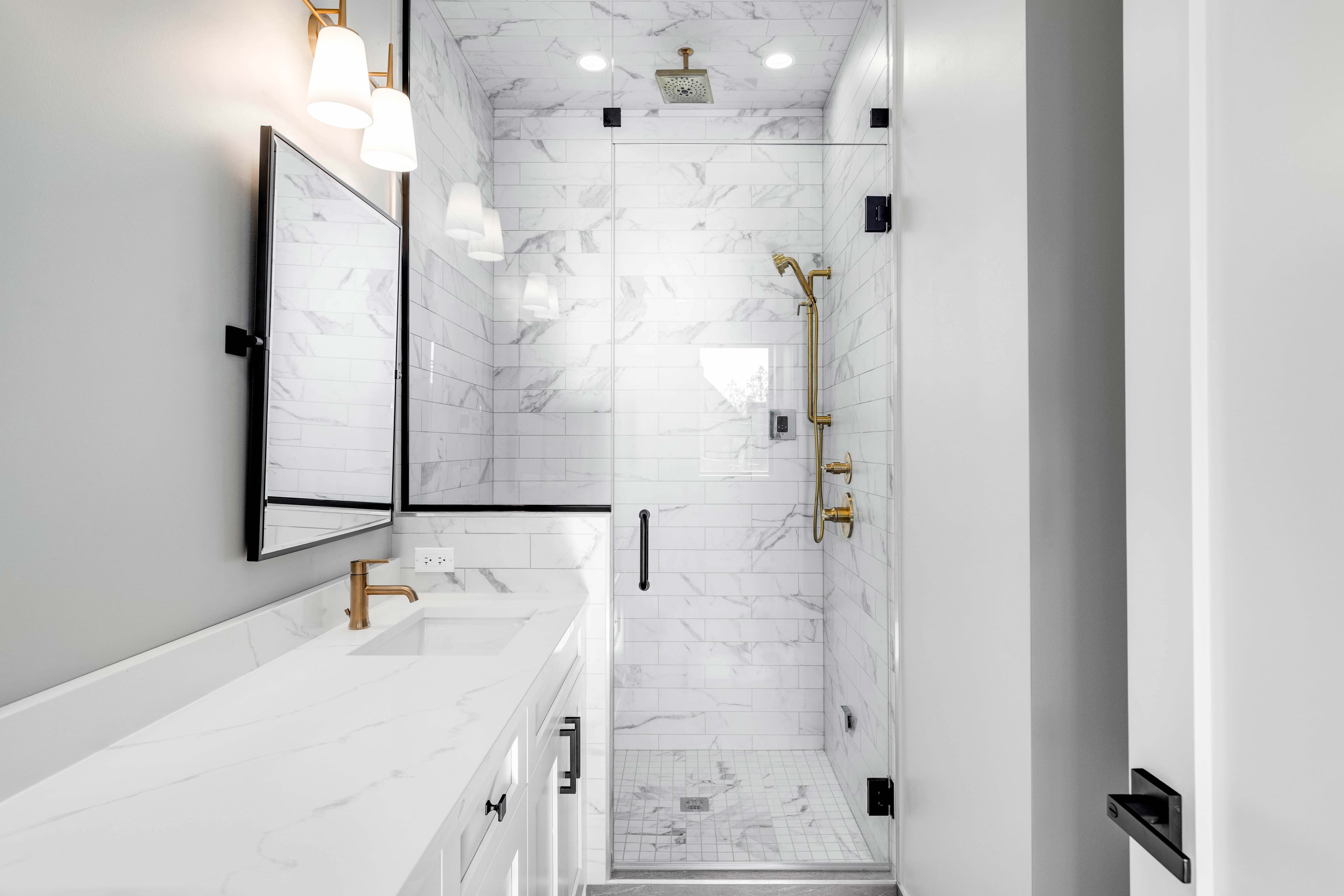 Modern bathroom featuring custom shower doors, marble tile, dual mirrors, and a sleek white countertop, showcasing the elegance of tempered glass and beveled glass edges.