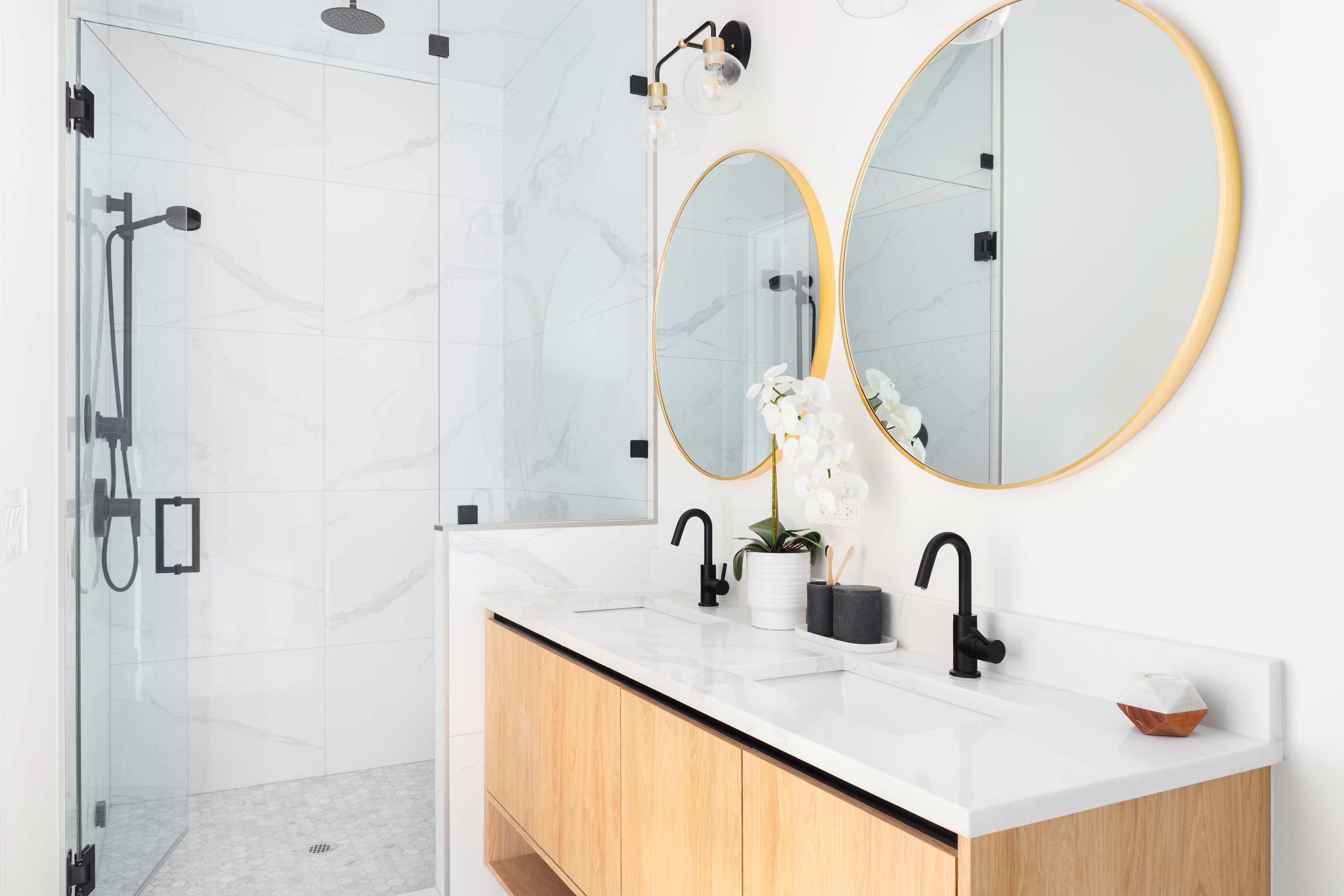 Modern bathroom featuring custom glass shower doors, elegant round mirrors with beveled glass edges, a sleek countertop, and minimalistic decor, highlighting tempered glass elements.