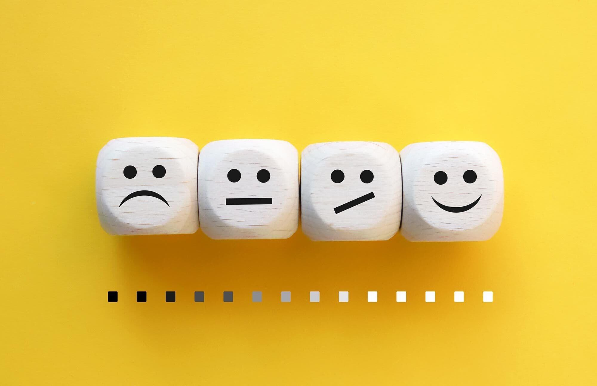Wooden blocks displaying varying facial expressions on a yellow background, symbolizing customer satisfaction and feedback for custom glass products like shower doors, table tops, mirrors, tempered glass, and beveled glass edges.