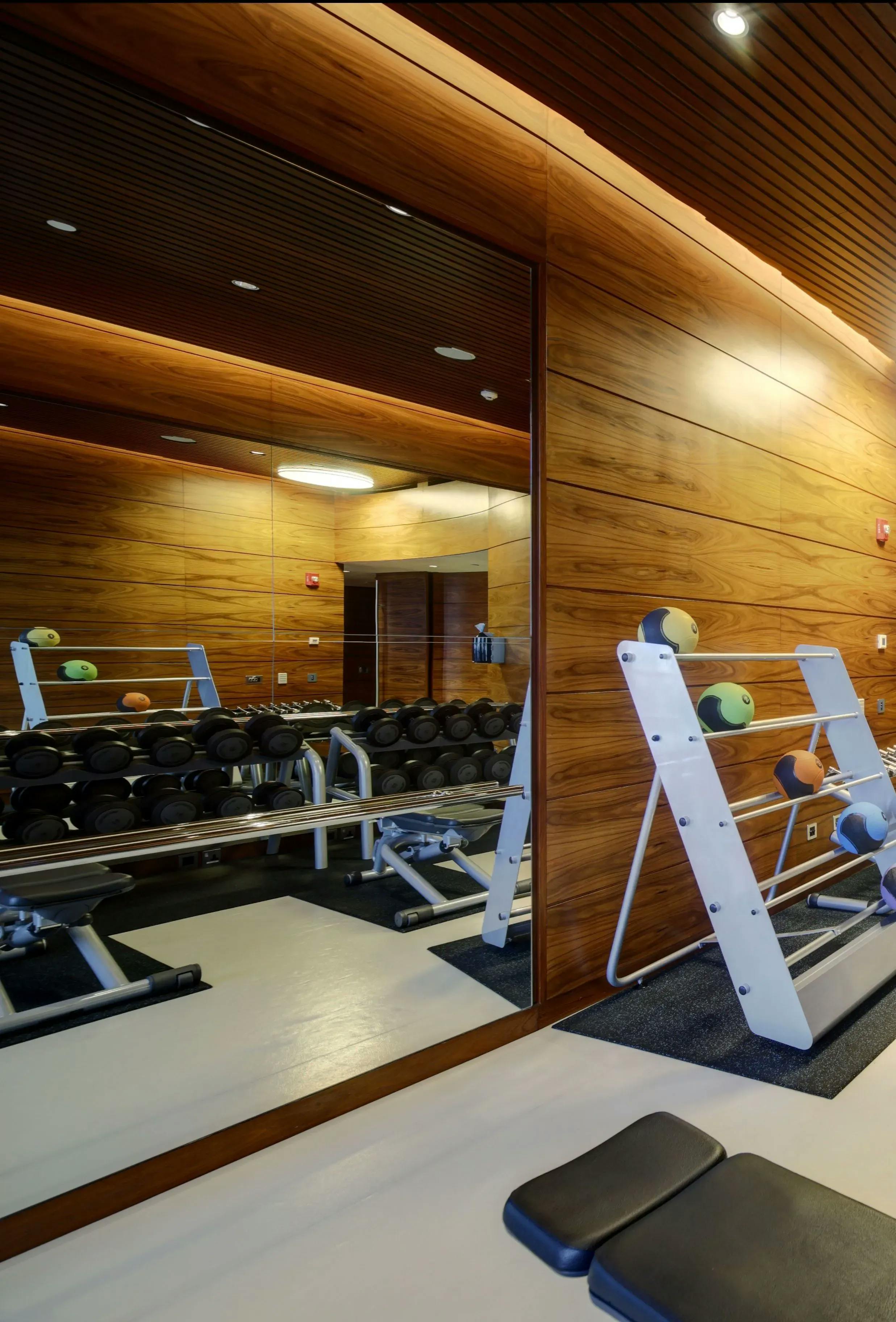 Gym setting with a focus on the gym mirror mounted on a wood wall, reflecting various gym equipment.