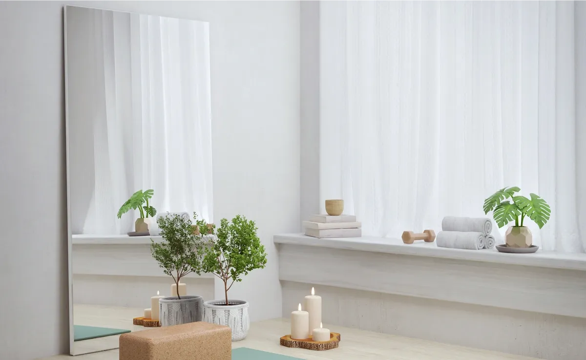 A yoga area with mat and block, sand and white colored room. rectangle mirror leans against the wall