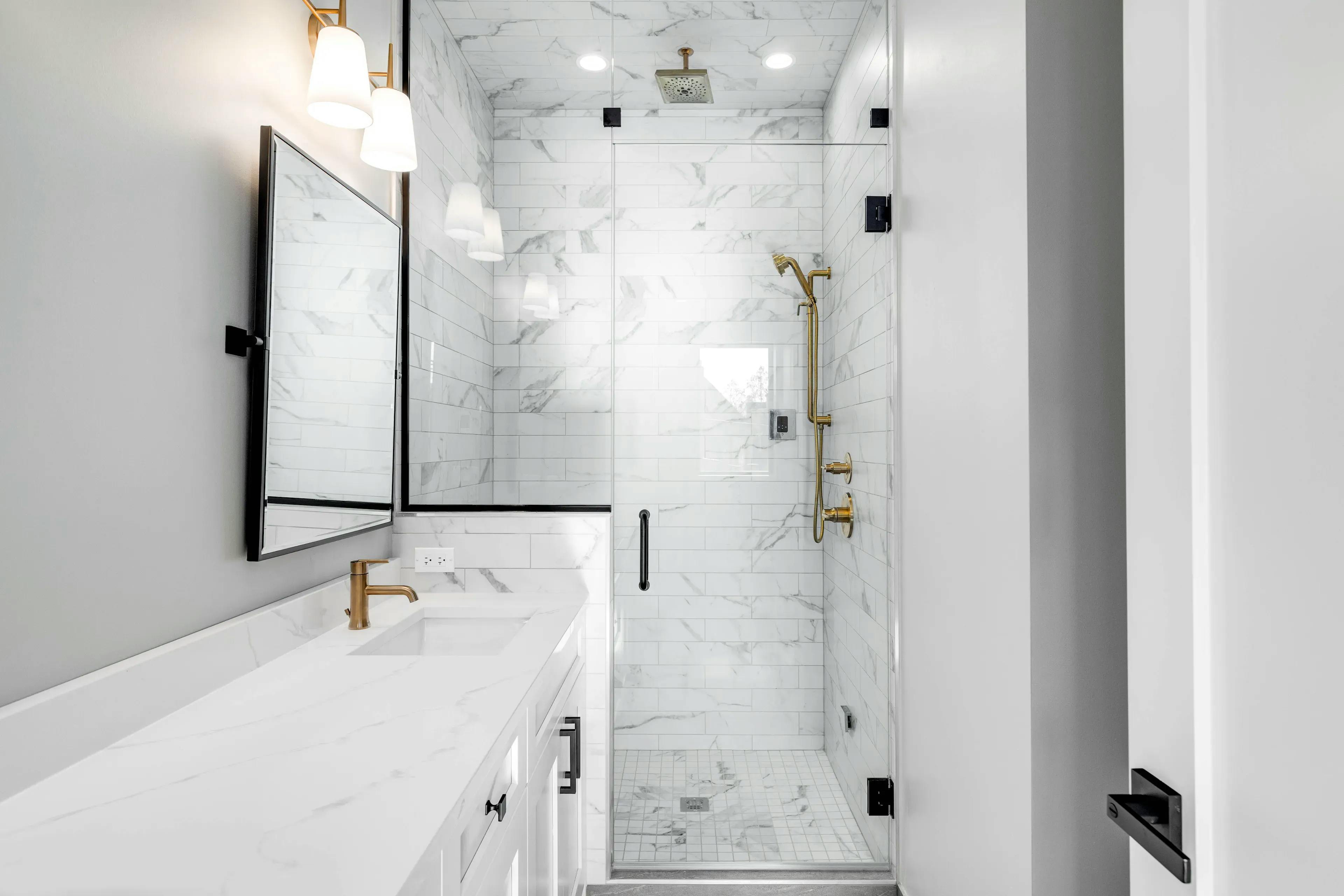 Small bathroom setting with glass shower doors. On one side, there's a sink and a rectangle mirror against white walls