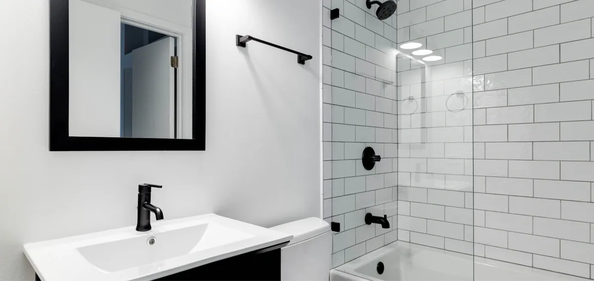 A monochrome bathroom with black and white tiled walls, featuring a white sink and a fixed bathtub glass panel with black matte hardware.