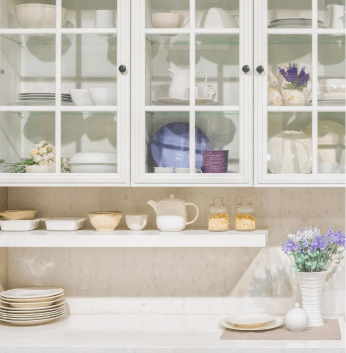 Kitchen setting with hanging cabinets featuring glass doors with plates and ceramics inside, along with a lower cabinet shelf holding small bowls