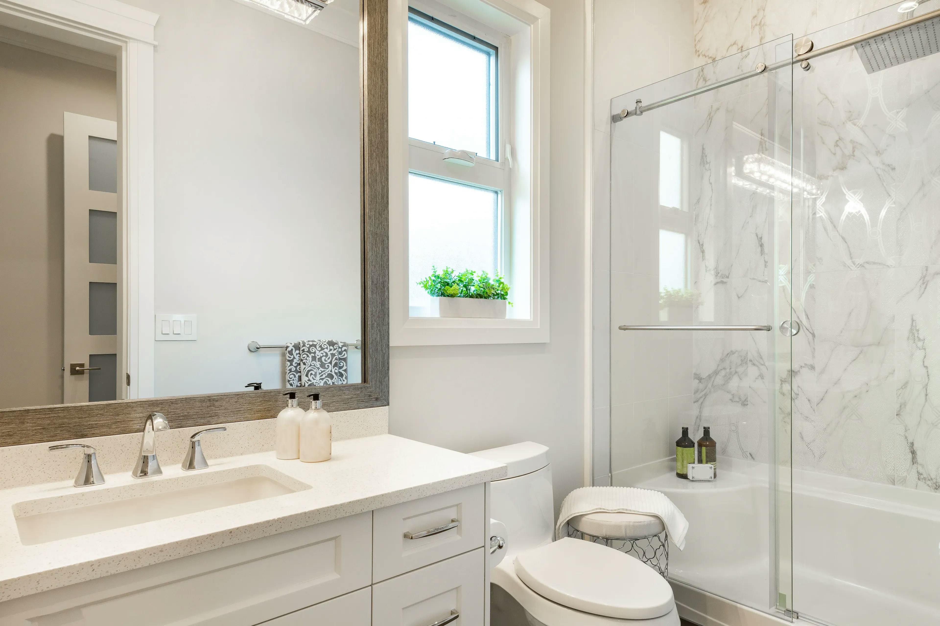 Bathroom setting with a vanity, mirror, sink, toilet seat, and sliding glass doors for the bathtub