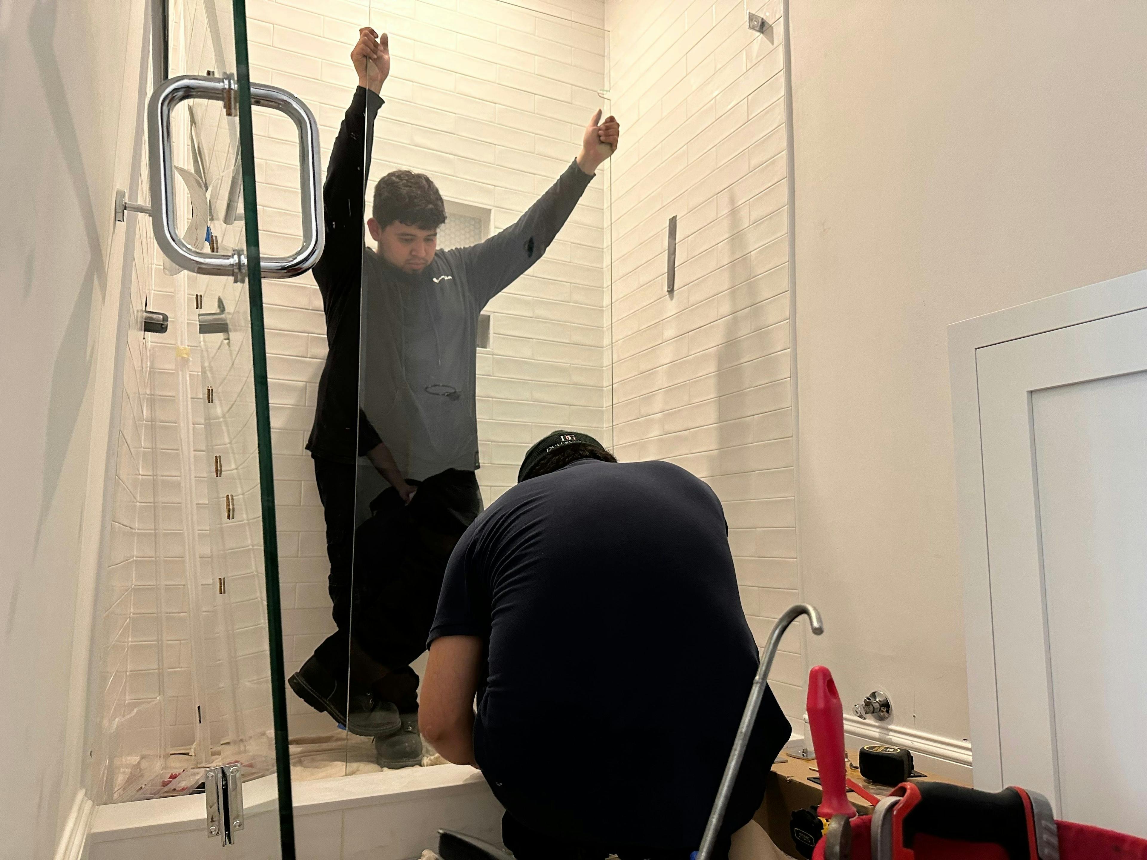 Two Dulles Glass workers, dressed in uniform, expertly installing a glass panel in a stylish white-tiled shower
