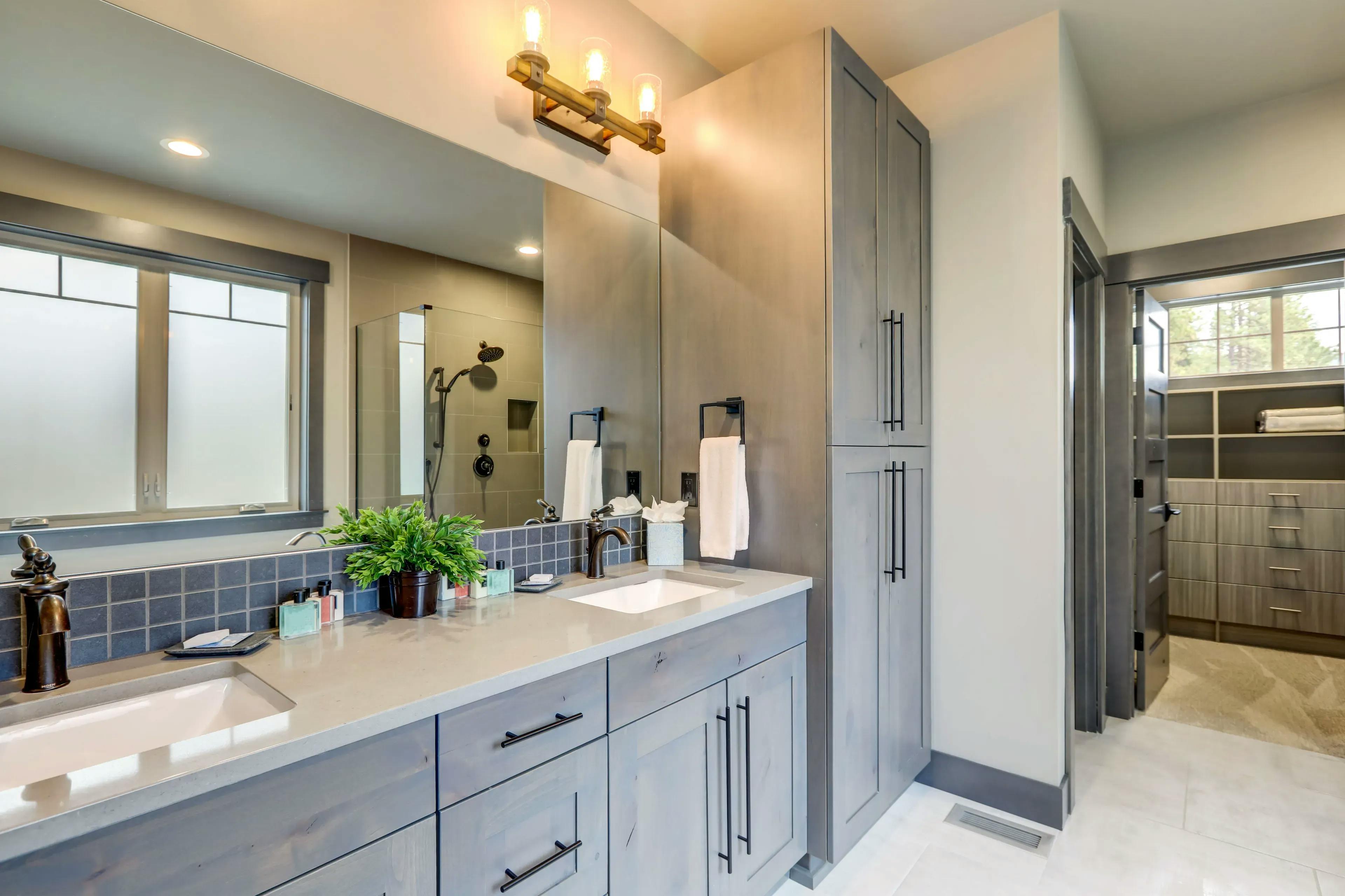 Bathroom setting with a large rectangular mirror over the sink, cabinets to one side, and a glass shower door in the background
