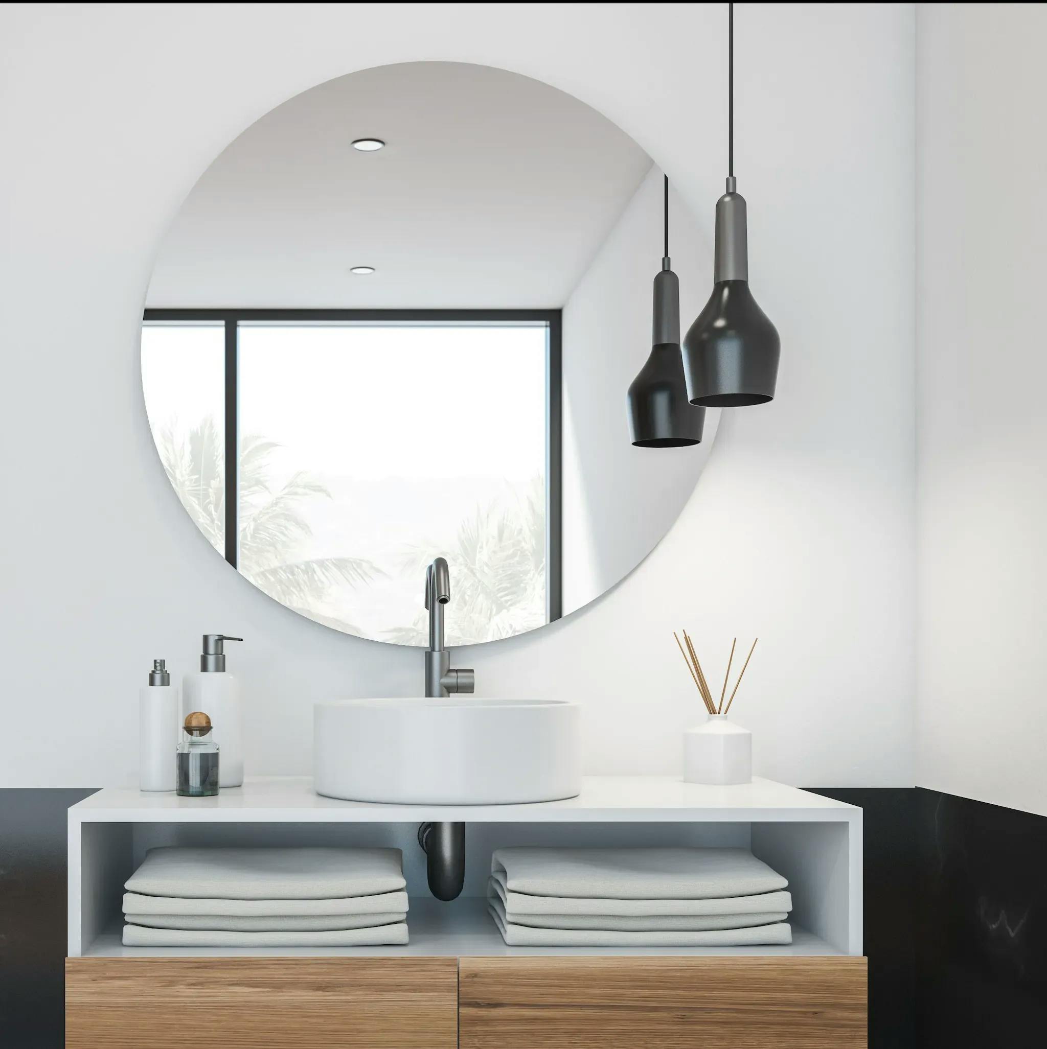 Round mirror on a bathroom vanity, with a sink in view and a hanging lamp suspended from the ceiling