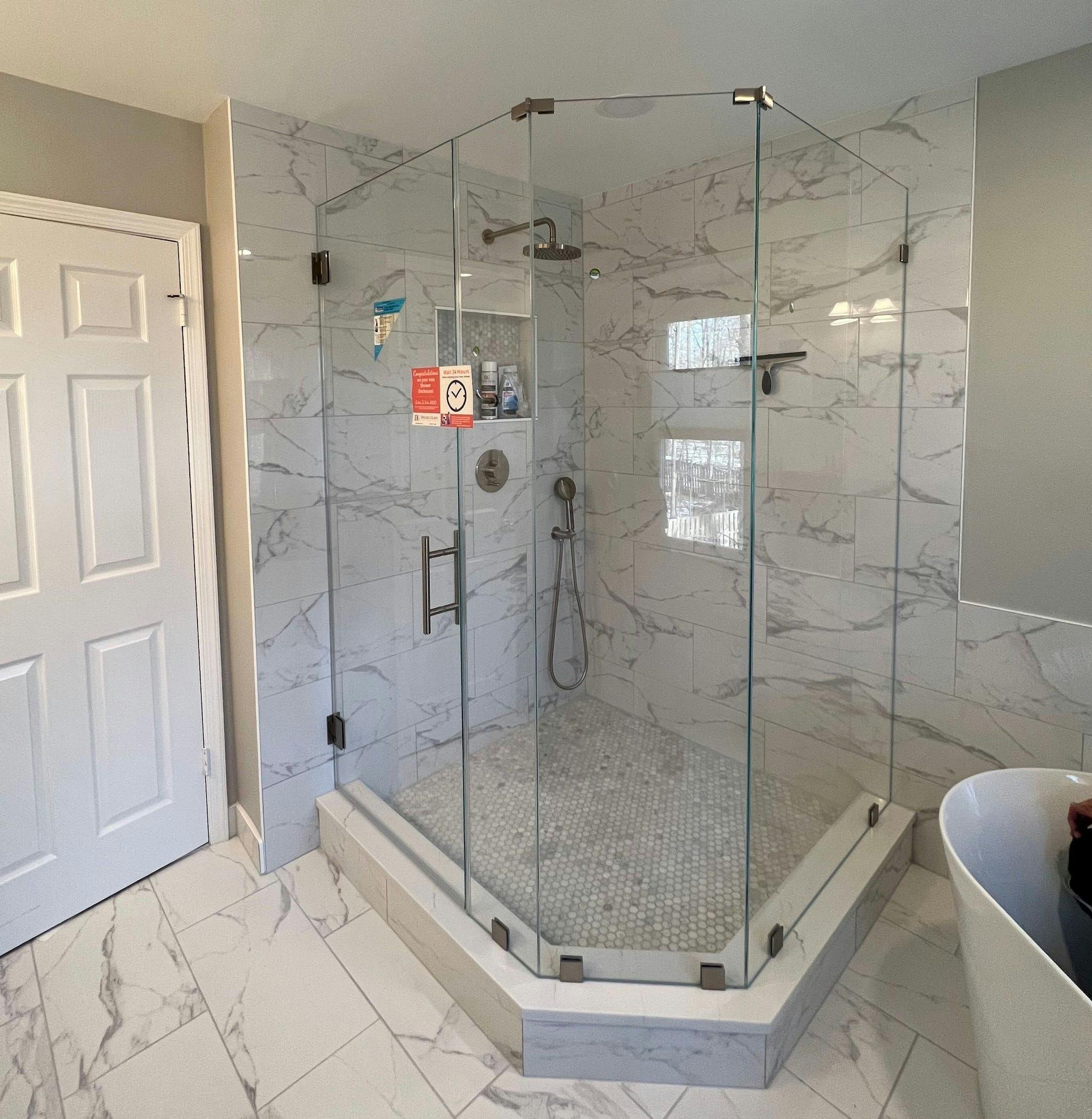 Large corner shower door enclosure with three sides, adjacent to a white door. The shower space and bathroom floor feature marble surfaces
