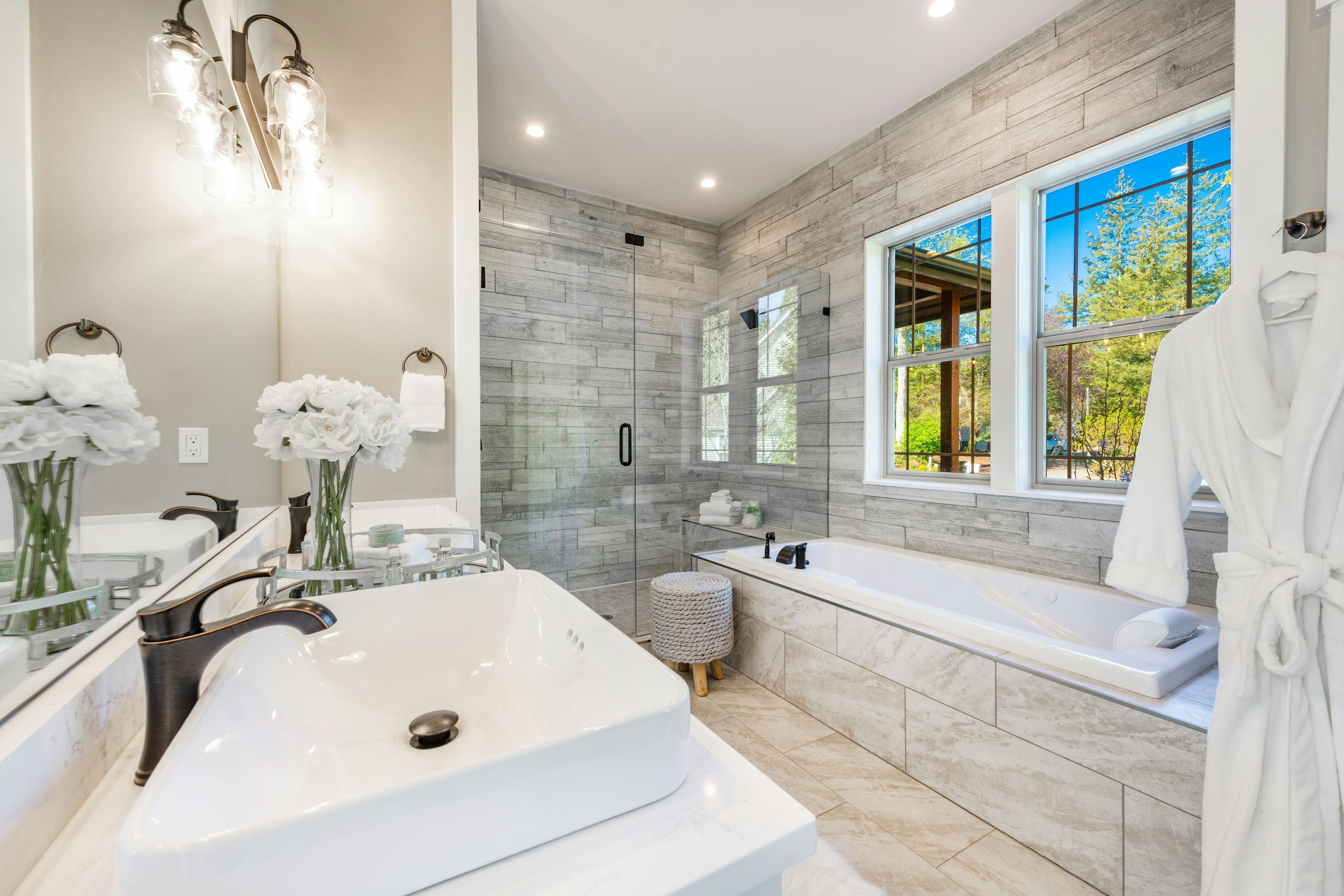 Bathroom setting with a view of the sink, bathtub, and a shower door in the background, with a window on one side