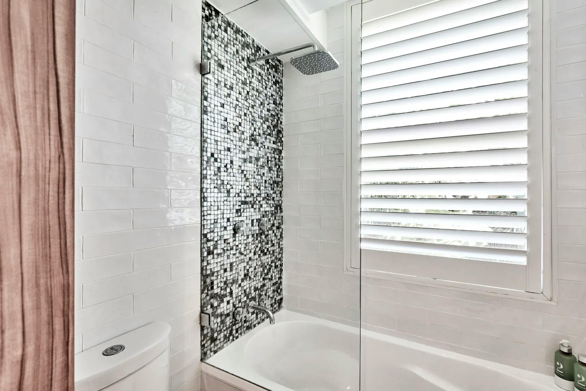 White bathroom, granite wall, bathtub with black and white speckle, window in enclosure, soap in corner.