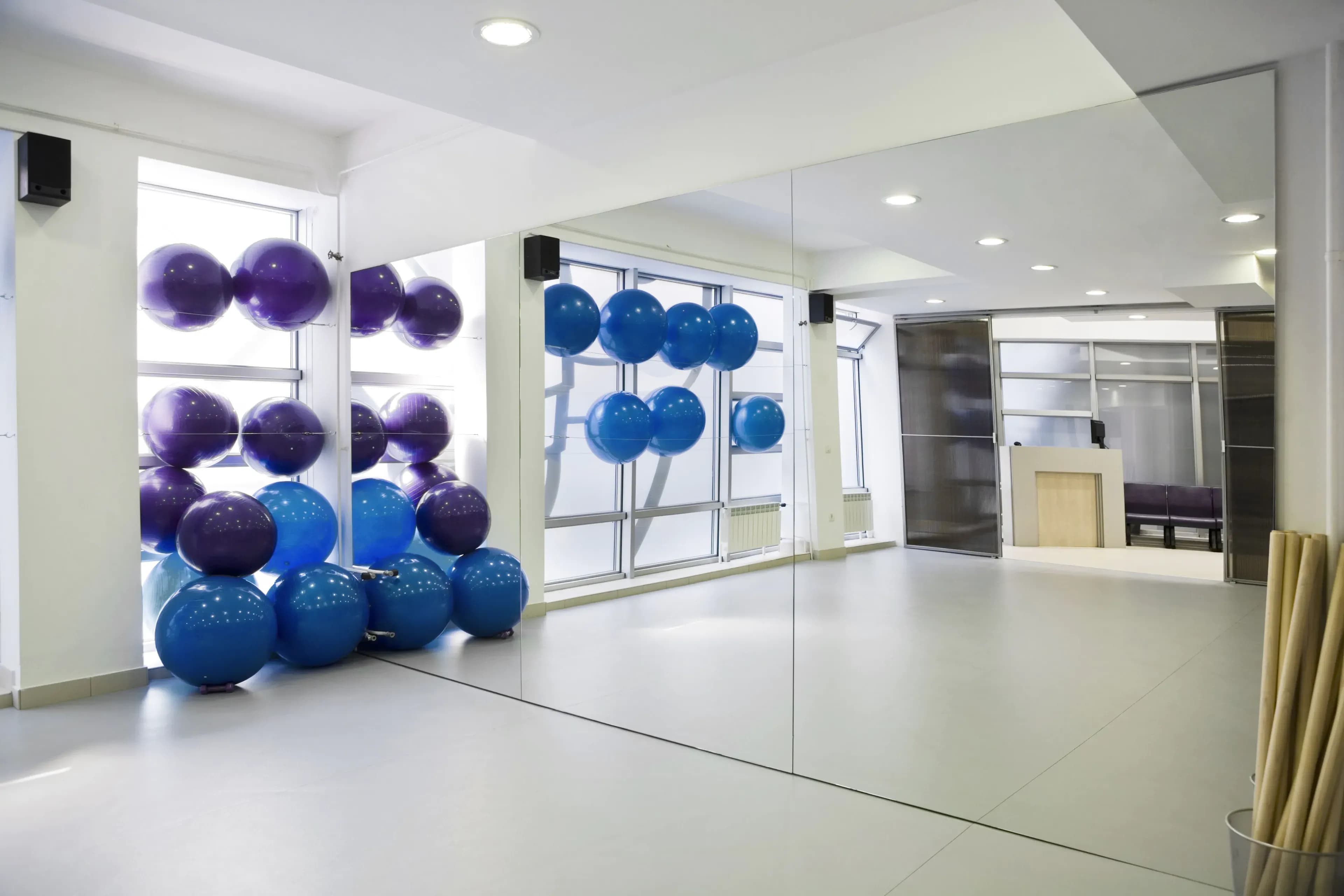Bright studio interior featuring large wall mirrors, colorful exercise balls, and modern design elements, showcasing custom glass solutions.