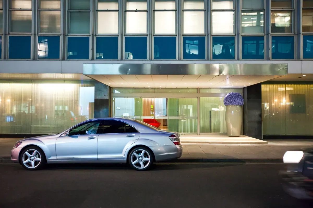Nighttime view of a modern building entrance with a sleek silver car parked outside, featuring large glass windows and a contemporary aesthetic, highlighting custom glass design elements.