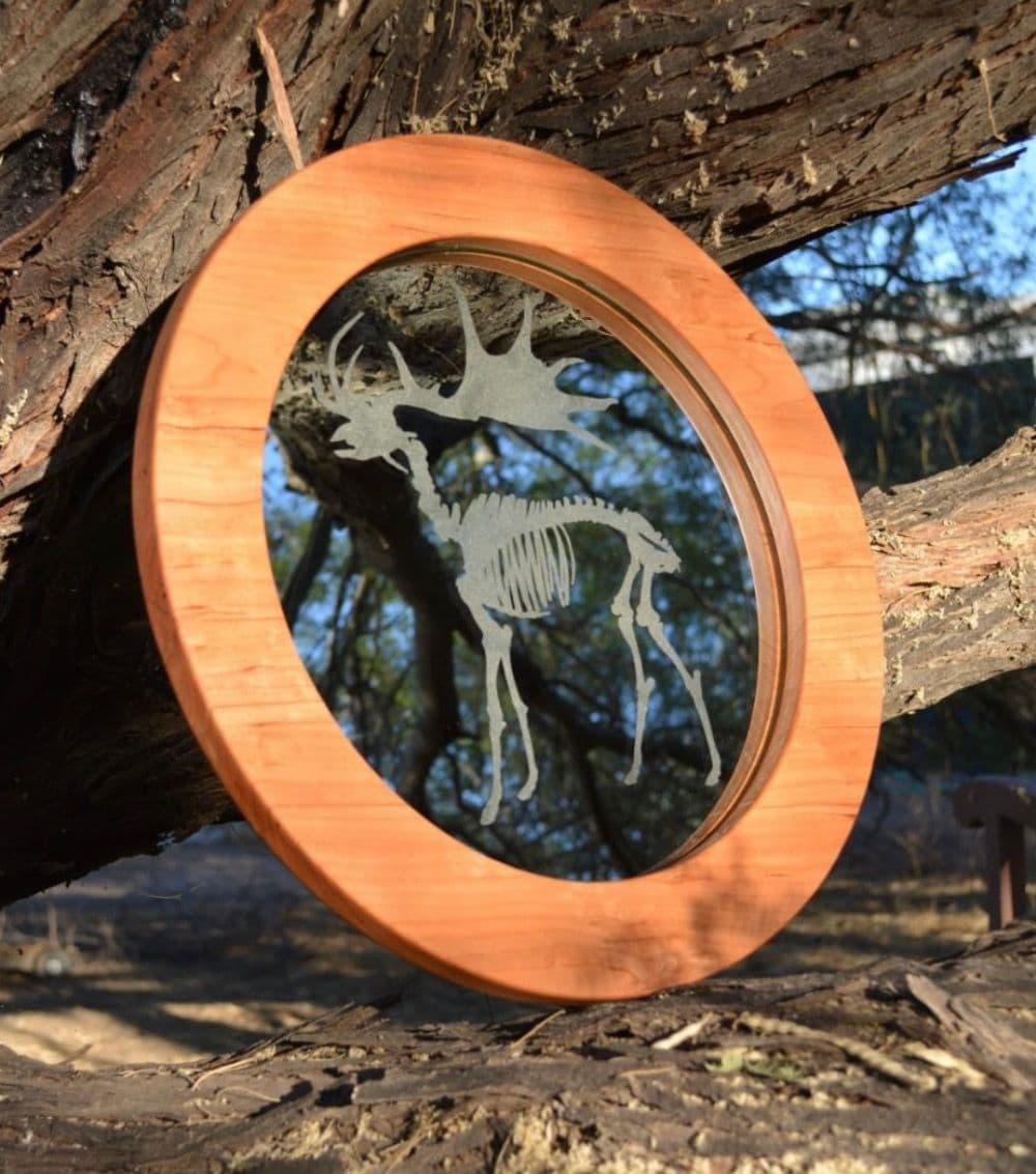 Custom round mirror with a carved elk skeleton design, featuring a wooden frame, ideal for unique dÚcor, complementing shower doors, table tops, and tempered glass applications.