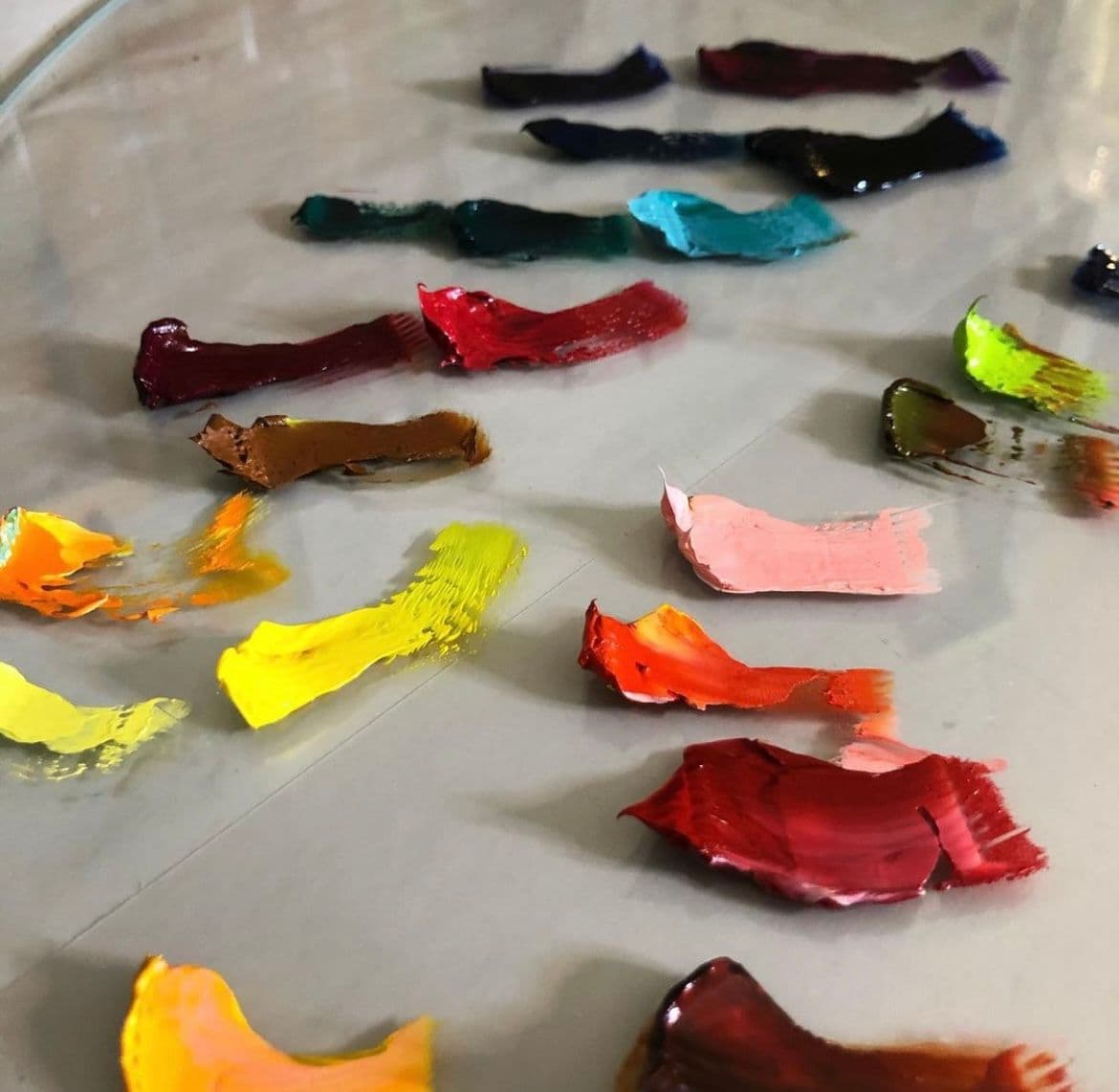 Colorful paint swatches arranged on a glass surface, showcasing creative potential for custom glass projects such as shower doors, table tops, and mirrors, emphasizing craftsmanship with tempered and beveled glass edges.