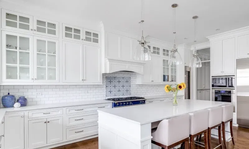 Modern kitchen featuring a white island with bar seating, custom glass cabinetry, and a bright aesthetic, highlighting the elegance of tempered glass surfaces and beveled glass edges.