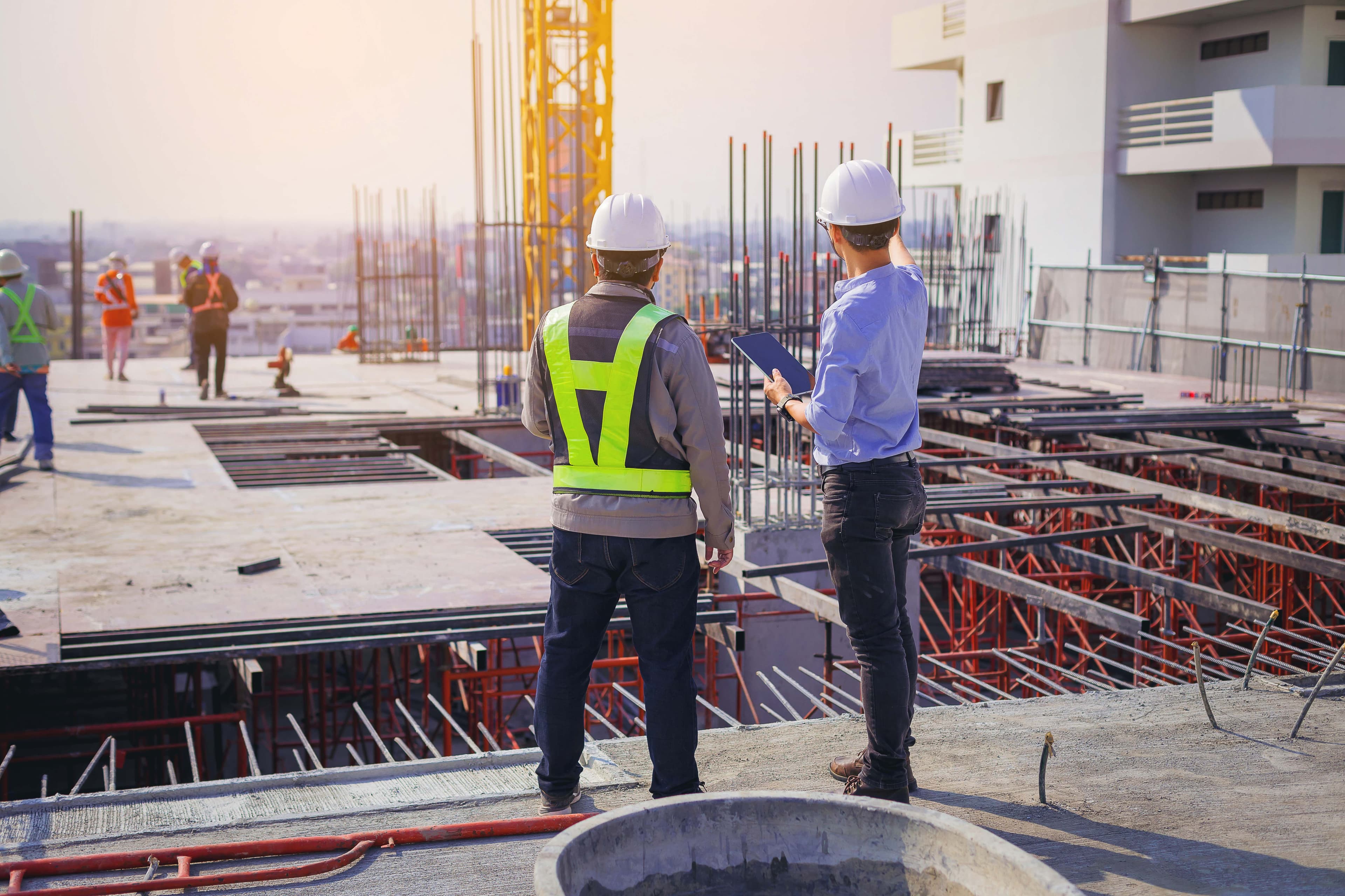 Construction workers discussing project plans on a building site with scaffolding and exposed rebar, emphasizing the importance of custom glass installations like shower doors and table tops.