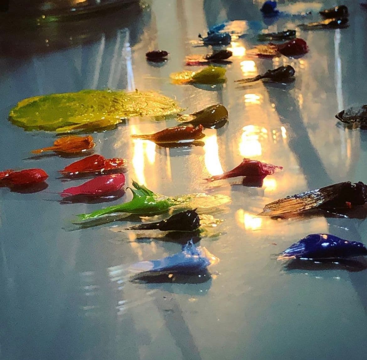 Colorful paint splatters on a glossy surface reflecting light, showcasing a creative workspace ideal for custom glass projects like shower doors, table tops, and mirrors.