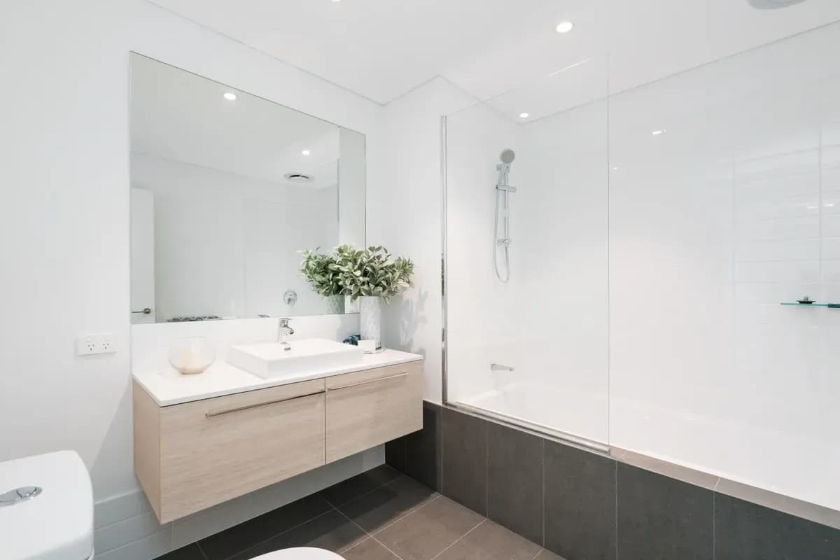 Modern bathroom featuring custom glass shower doors, a large wall mirror, and stylish storage with a sleek countertop, showcasing the elegance of tempered glass and beveled glass edges.