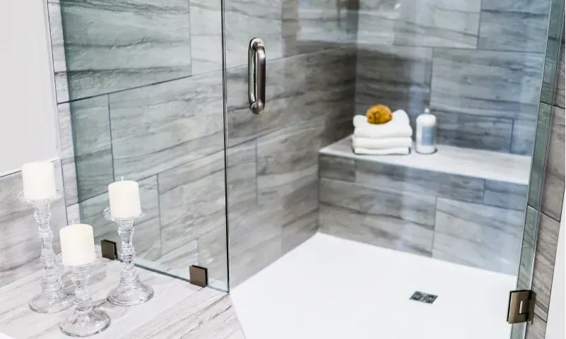 Modern shower door with tempered glass, showcasing a sleek design, accented by elegant candles and a minimalist aesthetic, emphasizing custom glass solutions for bathrooms.