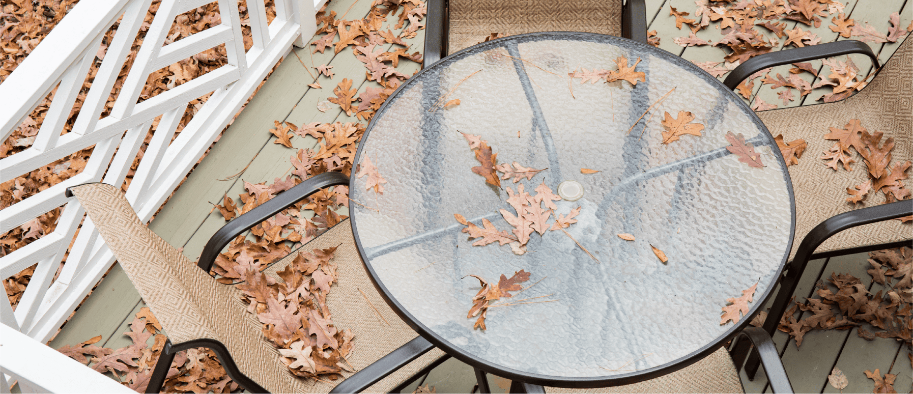 A frosted round glass table and chairs on a deck with leaves on it.