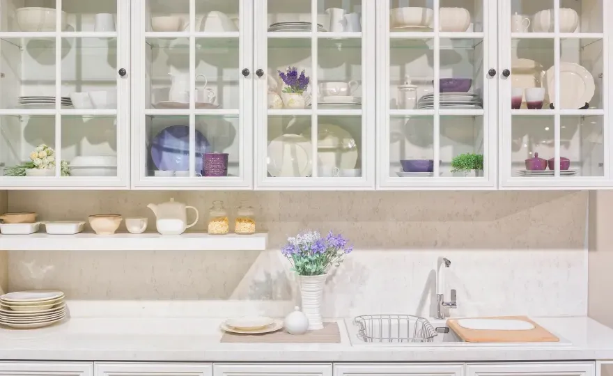 Modern kitchen interior featuring glass-front cabinets displaying dinnerware, complemented by a sleek countertop, ideal for showcasing custom glass solutions like tempered glass surfaces and mirrors.