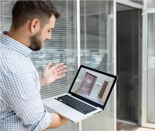 Man showing a laptop screen with an image of custom glass installations including shower doors, mirrors, and table tops in a modern setting, emphasizing tempered and beveled glass edges.