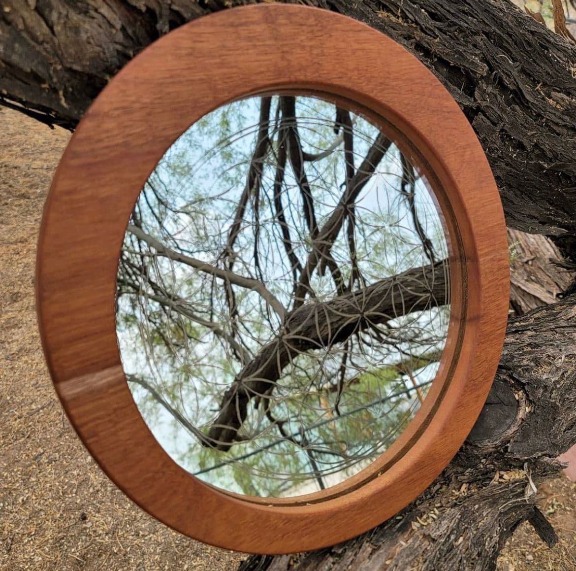 Round mirror with a wooden frame, reflecting tree branches, showcasing custom glass design and craftsmanship, ideal for decorative applications in homes.