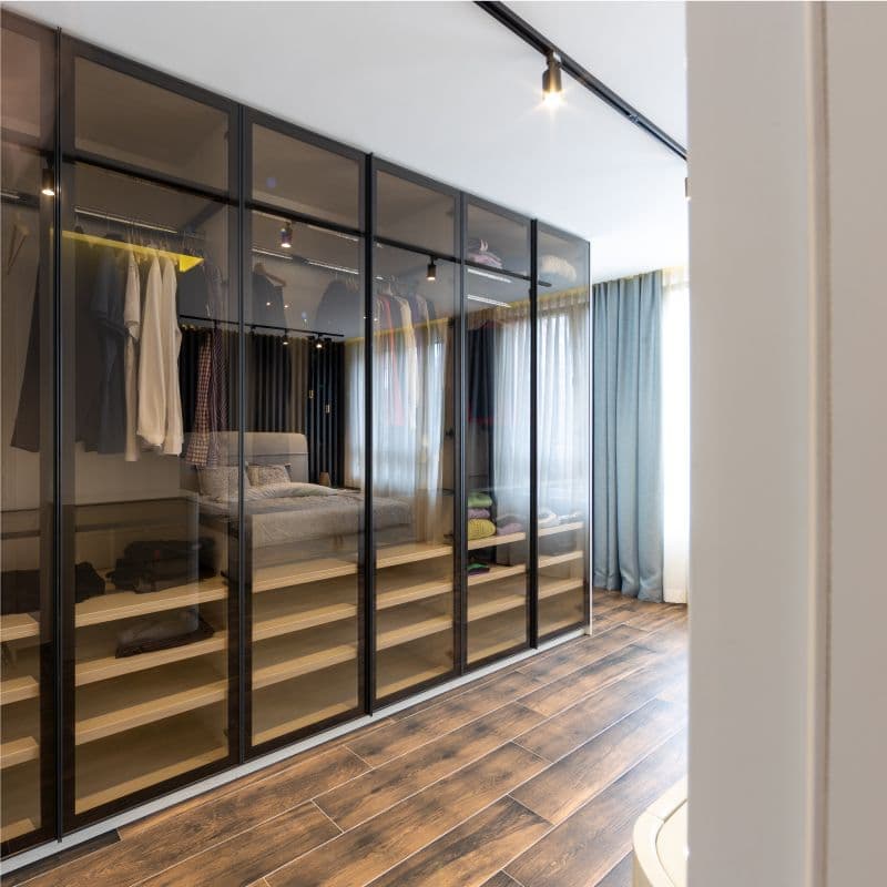 Modern bedroom with custom glass sliding doors showcasing organized clothing, highlighting tempered glass finishes and sleek design elements.