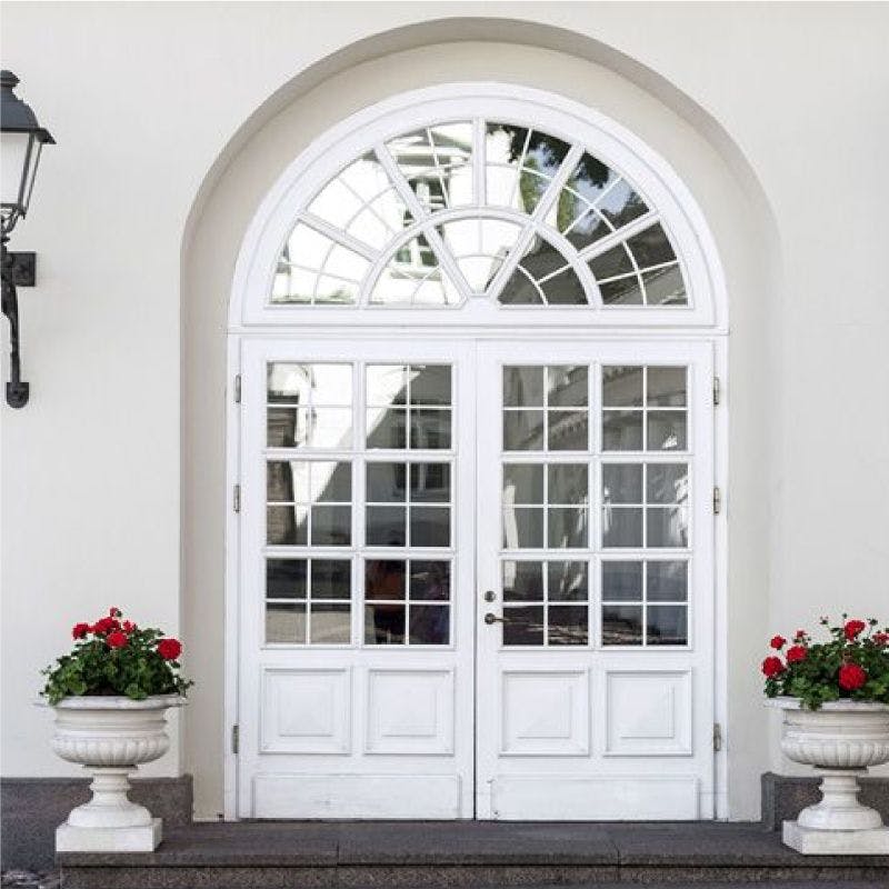 White double doors with glass inserts, adorned with vibrant red flowers in pots