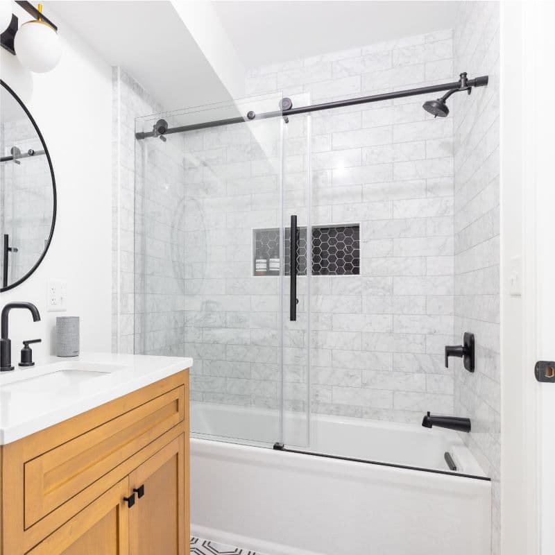 Custom glass shower doors, including tempered glass with a sleek design, paired with a stylish round mirror and modern bathroom vanity, showcasing elegant finishes in a contemporary bathroom setting.