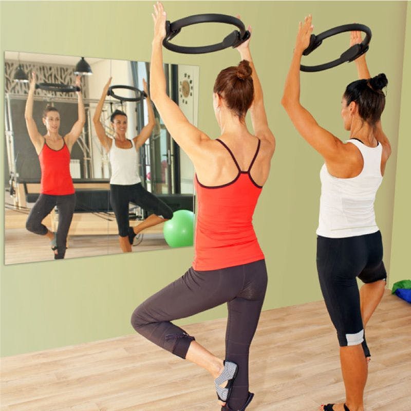Two women performing ring exercises in a gym in front of gym mirror